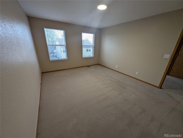 spare room featuring light carpet and baseboards