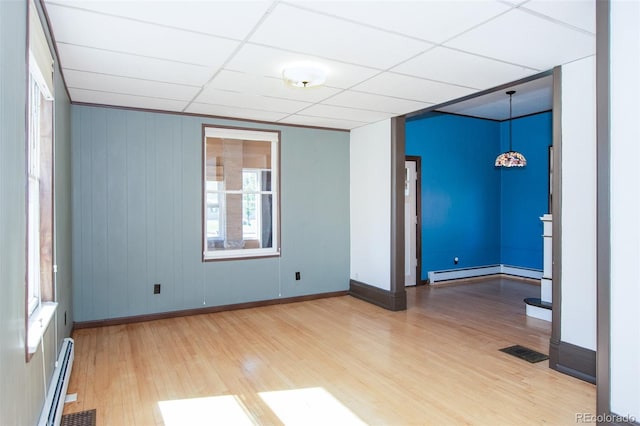 unfurnished room featuring wood-type flooring, a drop ceiling, and a baseboard heating unit