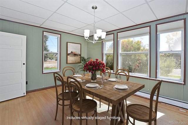 dining space featuring light wood-type flooring, a paneled ceiling, a baseboard radiator, and an inviting chandelier