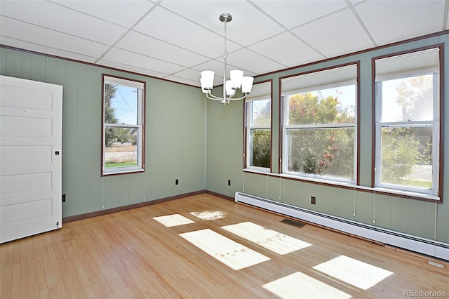 unfurnished dining area with a paneled ceiling, an inviting chandelier, a healthy amount of sunlight, and a baseboard heating unit