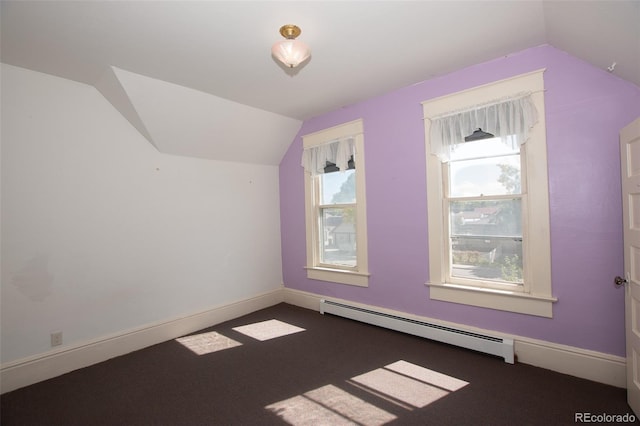 additional living space featuring dark carpet, vaulted ceiling, a wealth of natural light, and a baseboard heating unit