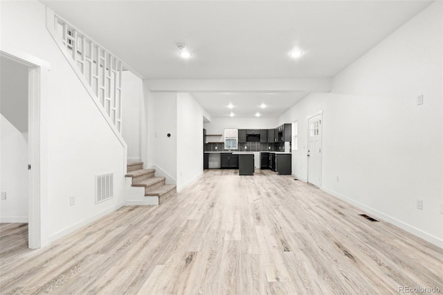 unfurnished living room featuring stairway, light wood finished floors, baseboards, and recessed lighting