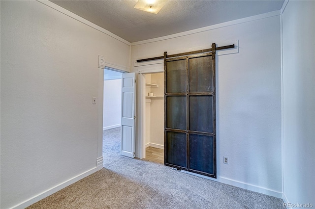 unfurnished bedroom with carpet flooring, a barn door, a textured ceiling, and a closet