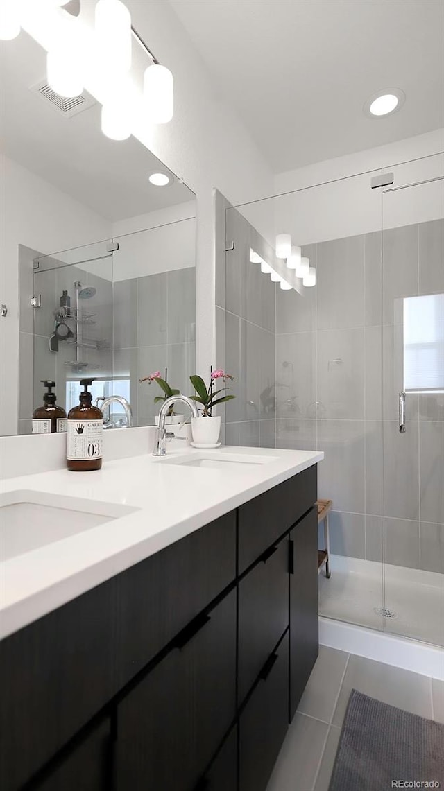 full bath with a sink, visible vents, a shower stall, tile patterned floors, and double vanity