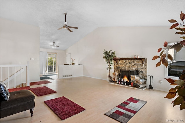 living area with visible vents, lofted ceiling, wood finished floors, a textured ceiling, and a stone fireplace