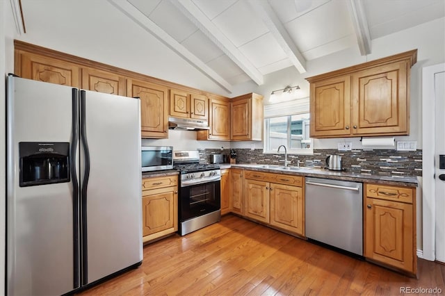 kitchen featuring vaulted ceiling with beams, under cabinet range hood, a sink, dark countertops, and appliances with stainless steel finishes