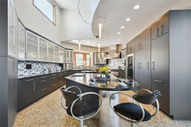 kitchen featuring wall chimney exhaust hood, sink, dark brown cabinets, and a kitchen island with sink