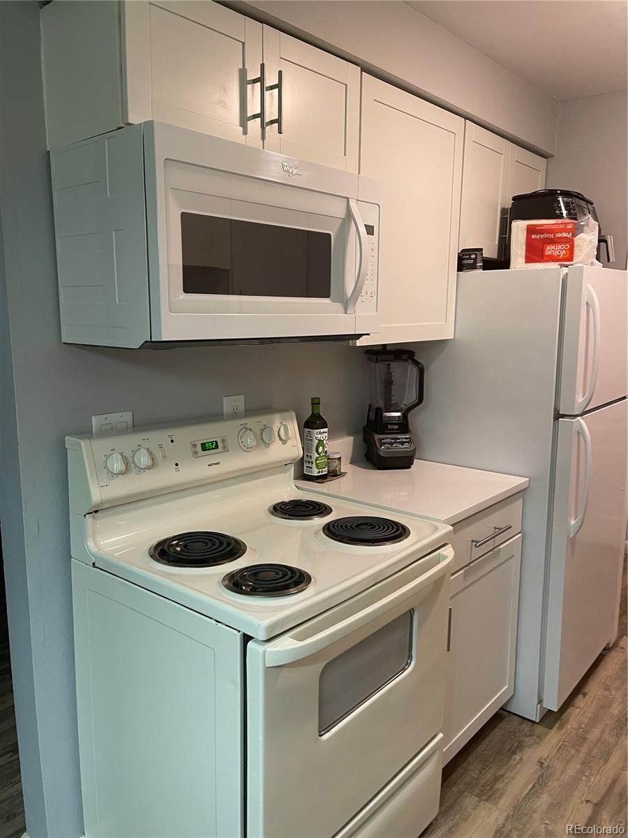 kitchen with white appliances, white cabinetry, wood finished floors, and light countertops