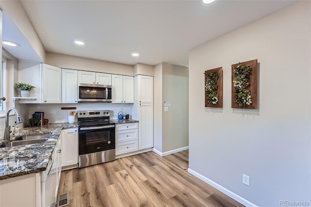 kitchen with stainless steel appliances, visible vents, white cabinetry, a sink, and dark stone counters