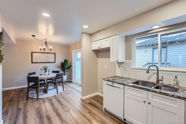 kitchen with backsplash, light wood-style floors, white dishwasher, a sink, and dark stone countertops