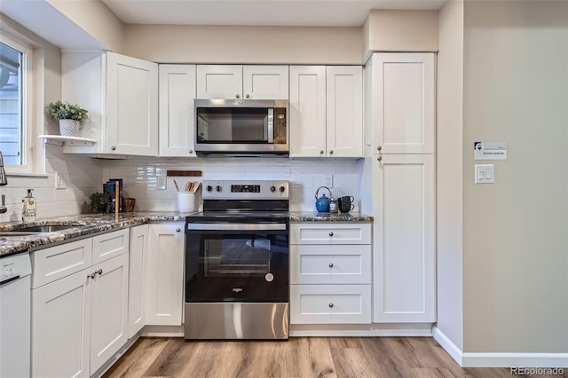 kitchen with stone counters, light wood finished floors, stainless steel appliances, backsplash, and white cabinetry