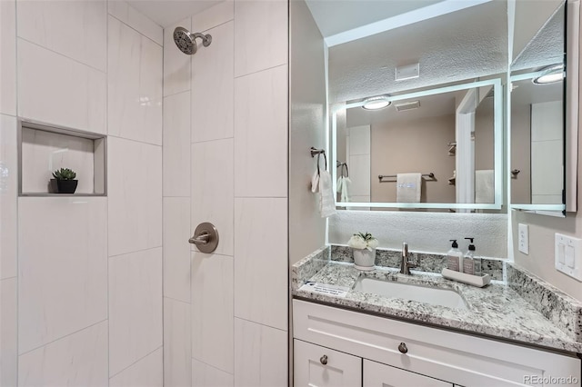 bathroom featuring visible vents, a tile shower, and vanity