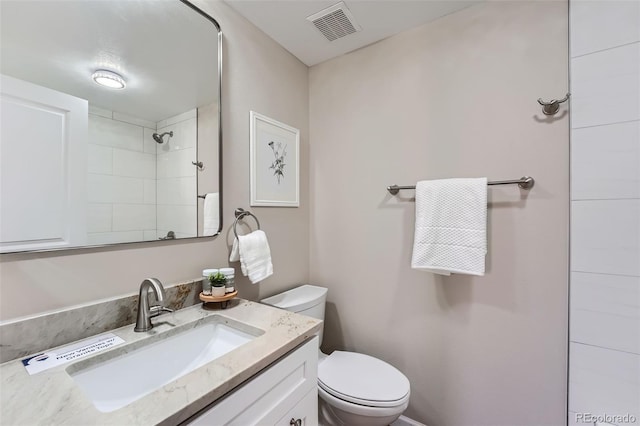 bathroom with toilet, tiled shower, vanity, and visible vents