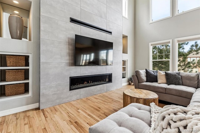 living room with a tiled fireplace, hardwood / wood-style floors, built in shelves, and a towering ceiling