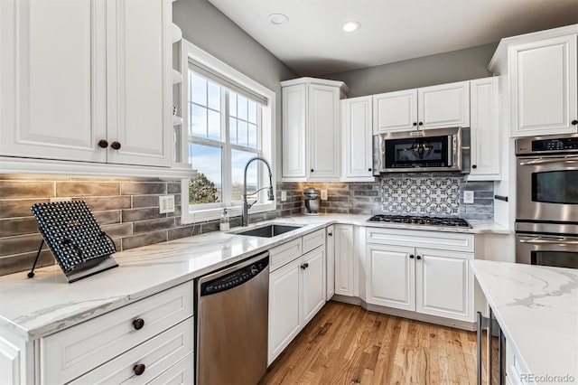 kitchen with sink, appliances with stainless steel finishes, white cabinetry, light stone countertops, and light wood-type flooring