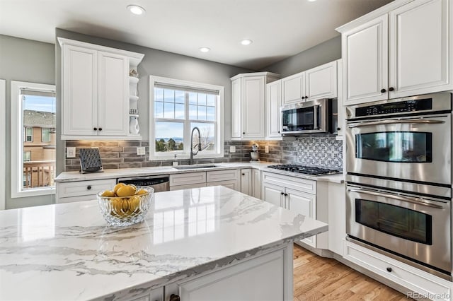 kitchen featuring sink, white cabinets, decorative backsplash, stainless steel appliances, and light stone countertops