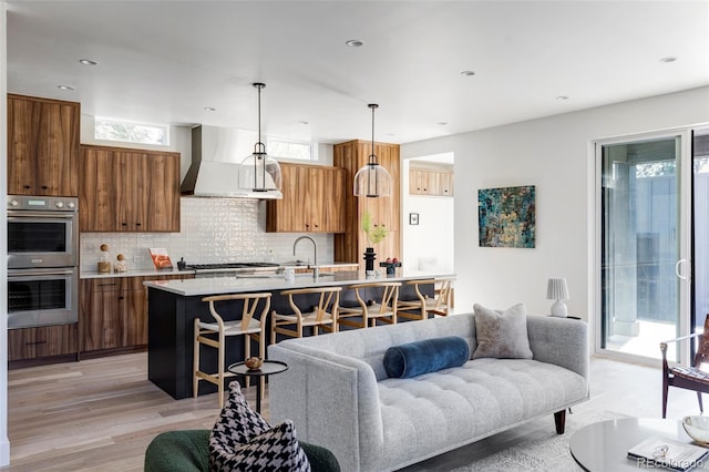 kitchen featuring appliances with stainless steel finishes, a breakfast bar, light hardwood / wood-style floors, wall chimney exhaust hood, and decorative light fixtures