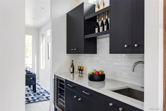 kitchen with decorative backsplash, light hardwood / wood-style flooring, sink, beverage cooler, and light stone counters