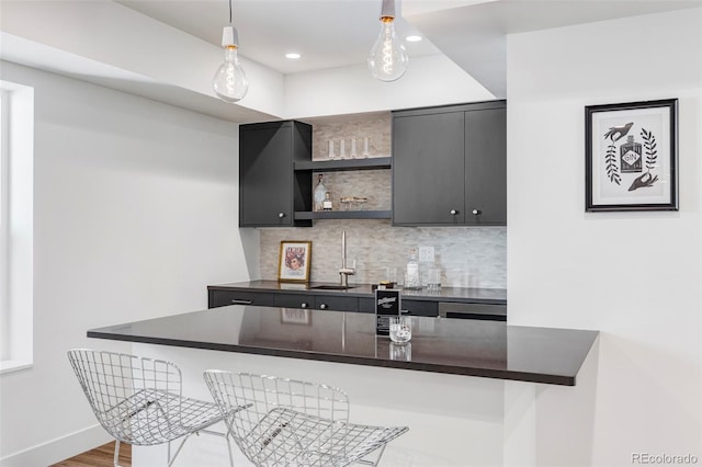 kitchen with kitchen peninsula, tasteful backsplash, hanging light fixtures, a breakfast bar, and hardwood / wood-style flooring