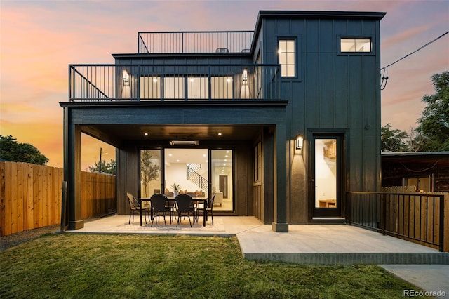 back house at dusk featuring a patio area, a lawn, and a balcony