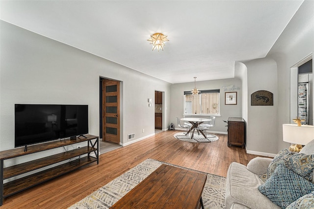 living area with hardwood / wood-style flooring, baseboards, visible vents, and an inviting chandelier