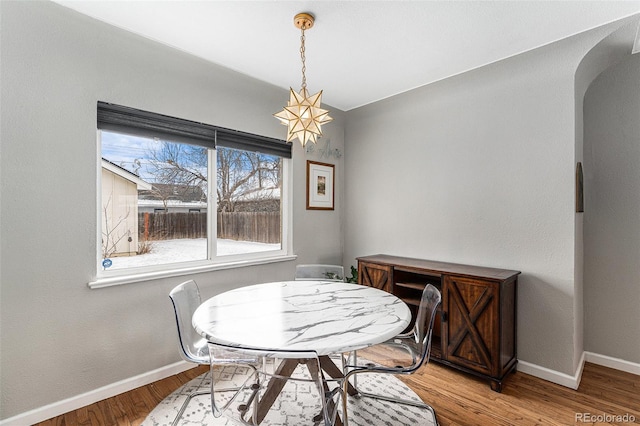 dining space featuring arched walkways, baseboards, and light wood-style floors