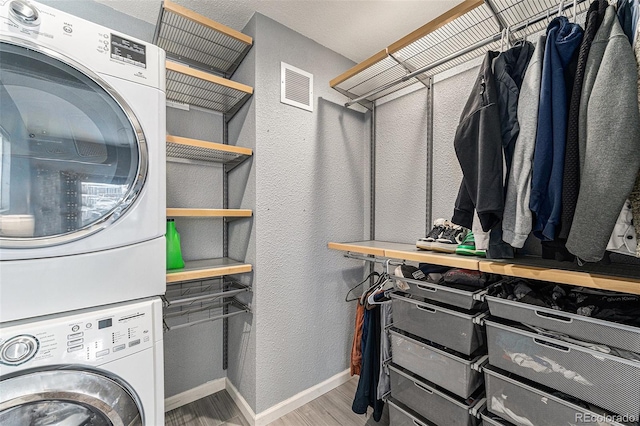 washroom with laundry area, baseboards, visible vents, stacked washer / dryer, and wood finished floors