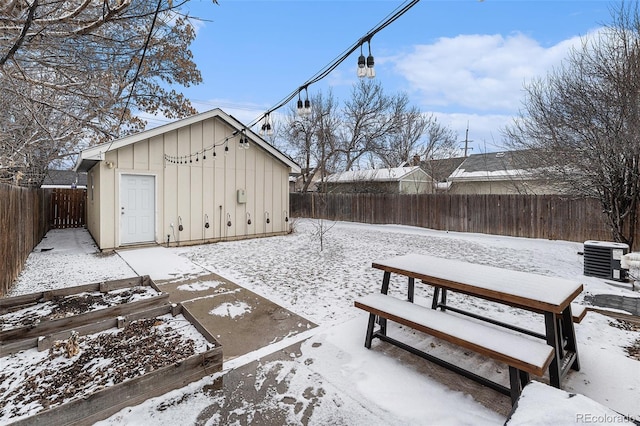 snowy yard with cooling unit, a fenced backyard, a vegetable garden, and an outbuilding