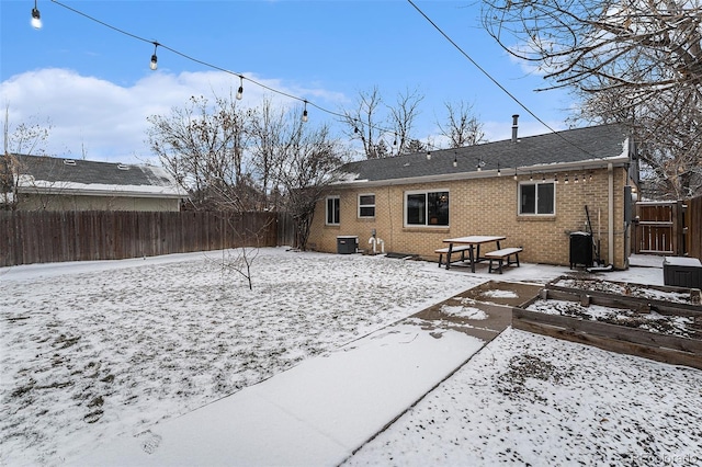 snow covered property featuring fence private yard, a patio area, cooling unit, and brick siding