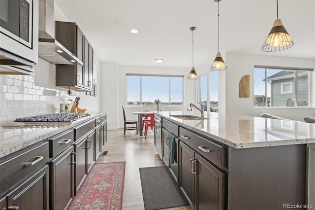 kitchen featuring wall chimney range hood, appliances with stainless steel finishes, a sink, and a wealth of natural light