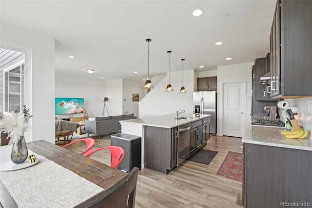 kitchen featuring dark brown cabinetry, appliances with stainless steel finishes, light wood-type flooring, a sink, and an island with sink