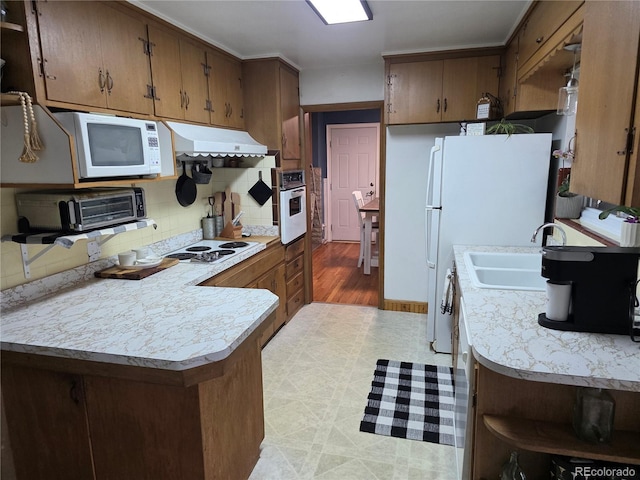 12375 W 19th Pl, Lakewood, CO 80215 - kitchen with under cabinet range hood, white appliances, light countertops, a peninsula, and decorative backsplash