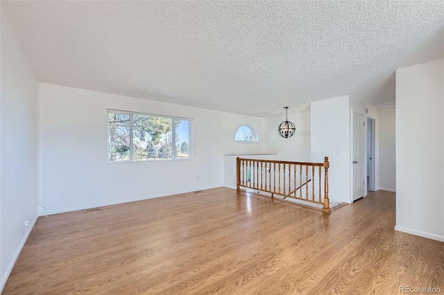 empty room with a textured ceiling, a chandelier, and light wood-type flooring