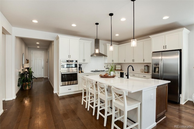 kitchen with stainless steel appliances, wall chimney exhaust hood, light countertops, and decorative backsplash