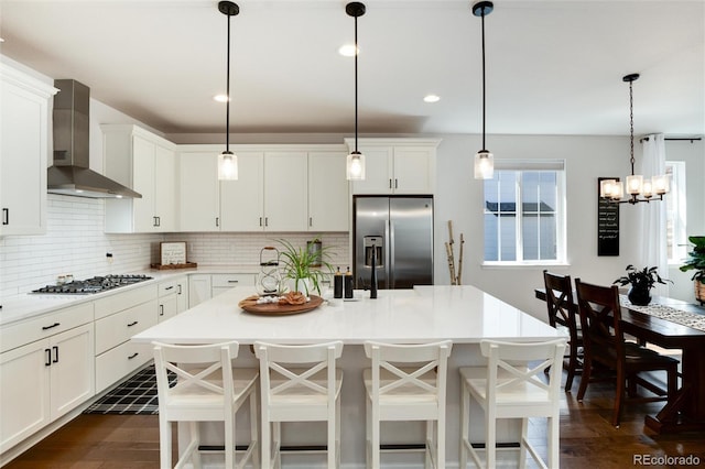 kitchen featuring wall chimney exhaust hood, dark wood-type flooring, white cabinetry, appliances with stainless steel finishes, and decorative backsplash