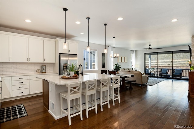 kitchen with stainless steel fridge with ice dispenser, tasteful backsplash, light countertops, a kitchen island with sink, and ceiling fan with notable chandelier