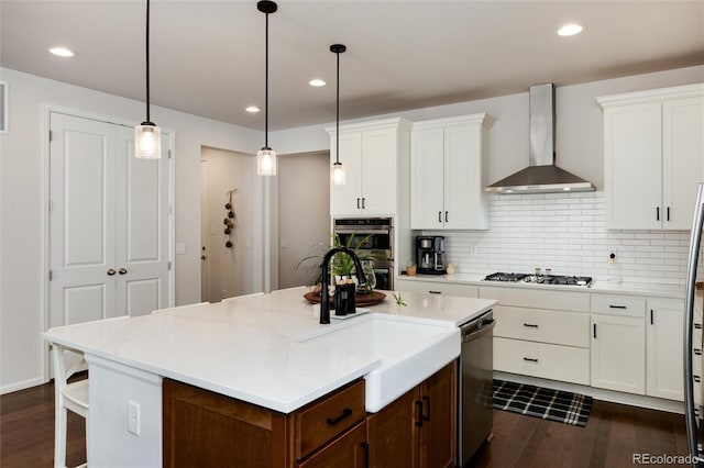 kitchen featuring white cabinets, a center island, wall chimney range hood, appliances with stainless steel finishes, and dark wood finished floors