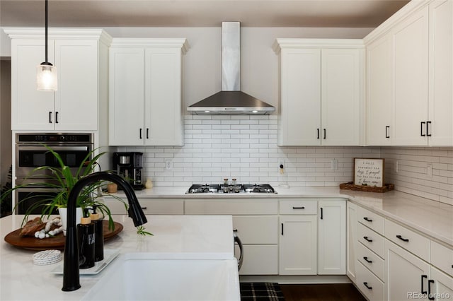 kitchen with white cabinets, wall chimney exhaust hood, a sink, light countertops, and appliances with stainless steel finishes