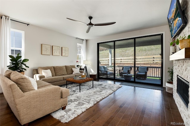 living area featuring dark wood-type flooring, ceiling fan, and a fireplace