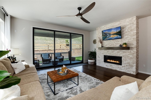 living area with baseboards, a stone fireplace, wood finished floors, and ceiling fan