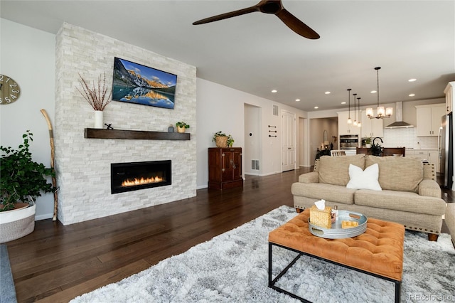 living area with baseboards, a fireplace, dark wood-type flooring, visible vents, and ceiling fan with notable chandelier