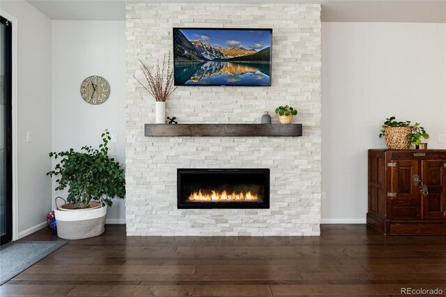 living room featuring baseboards, a stone fireplace, and hardwood / wood-style floors