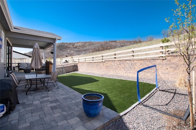 view of yard featuring a patio, outdoor dining area, a fenced backyard, and a mountain view