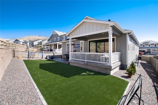 rear view of house featuring board and batten siding, a yard, a fenced backyard, and a residential view
