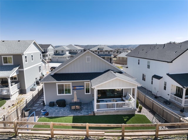 back of house with a patio area, board and batten siding, a fenced backyard, a residential view, and roof with shingles