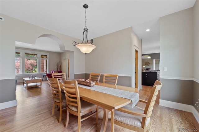 dining area with arched walkways, baseboards, recessed lighting, and light wood-type flooring