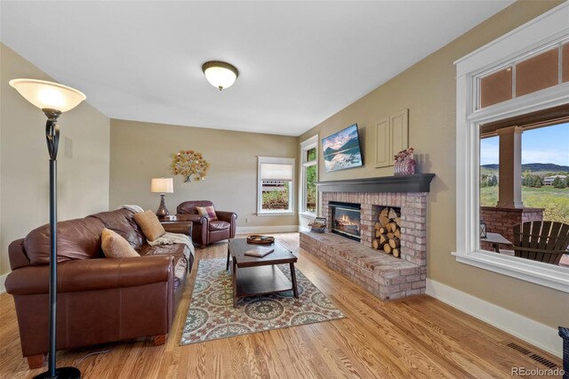 living area with a brick fireplace, visible vents, plenty of natural light, and wood finished floors