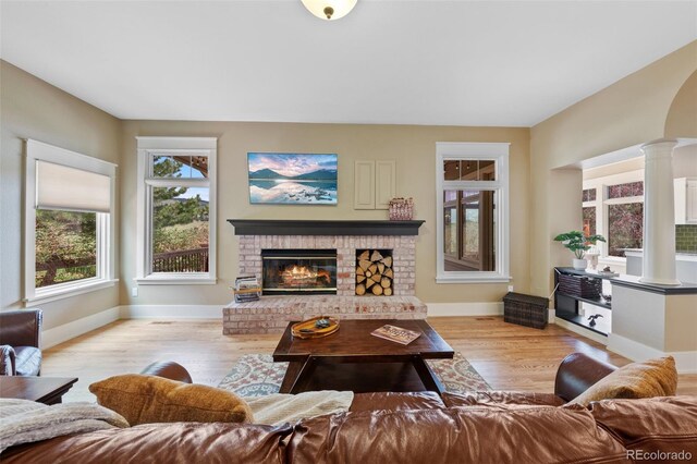 living area featuring baseboards, decorative columns, wood finished floors, and a brick fireplace