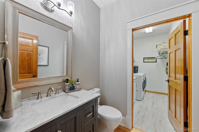 half bath with separate washer and dryer, toilet, wood finished floors, and vanity