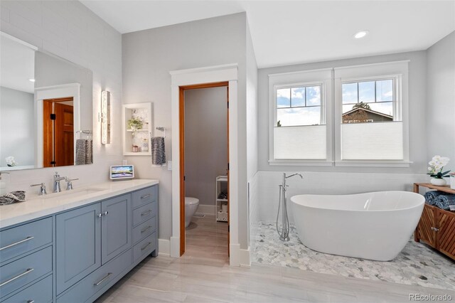 full bath with vanity, toilet, baseboards, recessed lighting, and a freestanding bath
